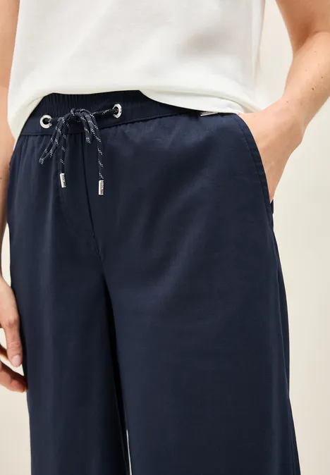 Person trägt eine weiße Bluse und eine dunkelblaue Hose mit Kordelzug.